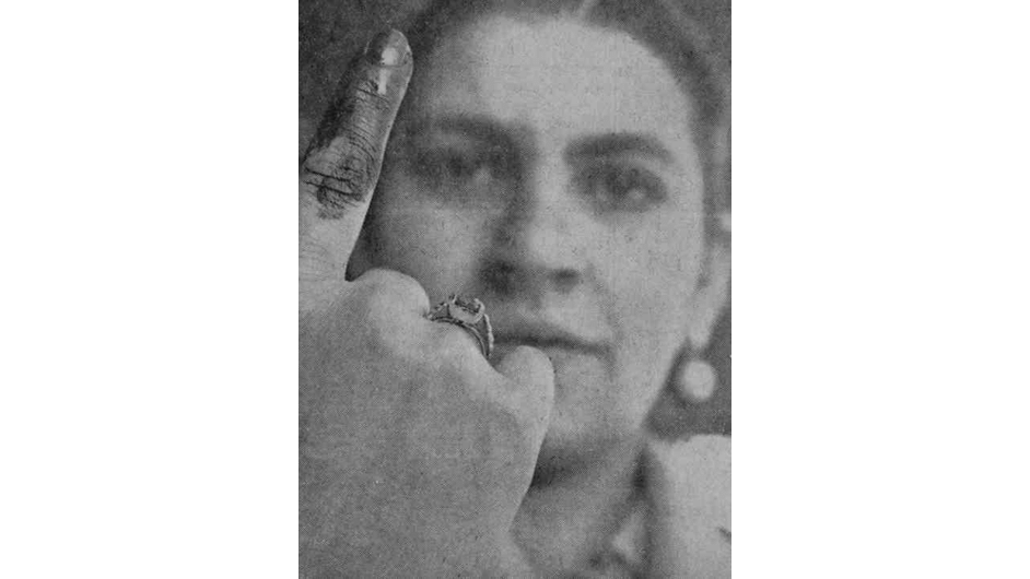 Fotografía histórica en blanco y negro de una mujer colombiana mostrando su dedo marcado con tinta indeleble tras votar por primera vez en el plebiscito de 1957